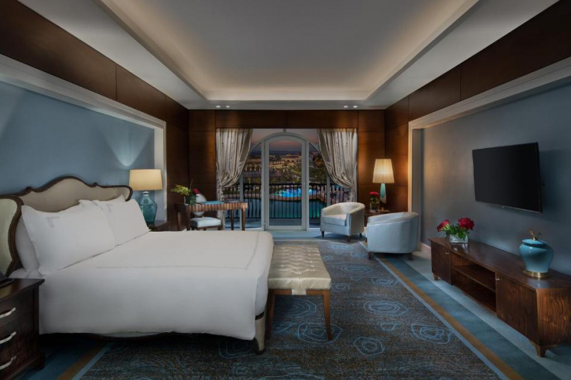 The spacious room has 1 king-sized bed with nightstands, a workstation and a chair, and 2 low-back armchairs. There is also a wall-mounted TV, a plush bed bench and a door leading onto the balcony.