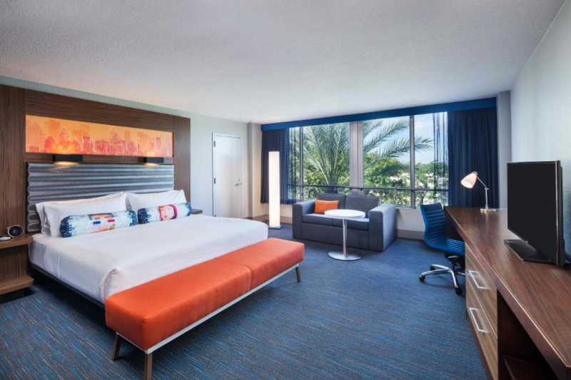 The spacious room has a king-sized bed with nightstands, and plush bed bench. There is a sofa bed with a coffee table and a workstation with a movable chair, cupboard and TV.