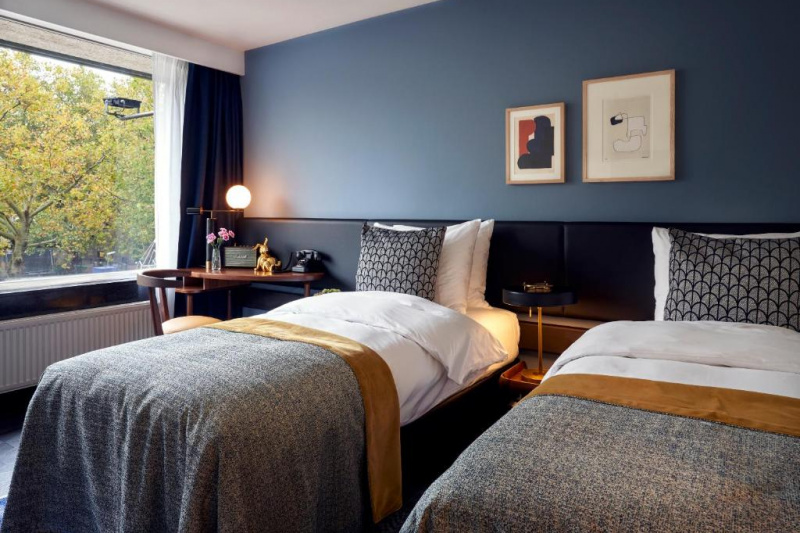 The room has twin beds with a central nightstand. There is a small table with a movable captain's chair.