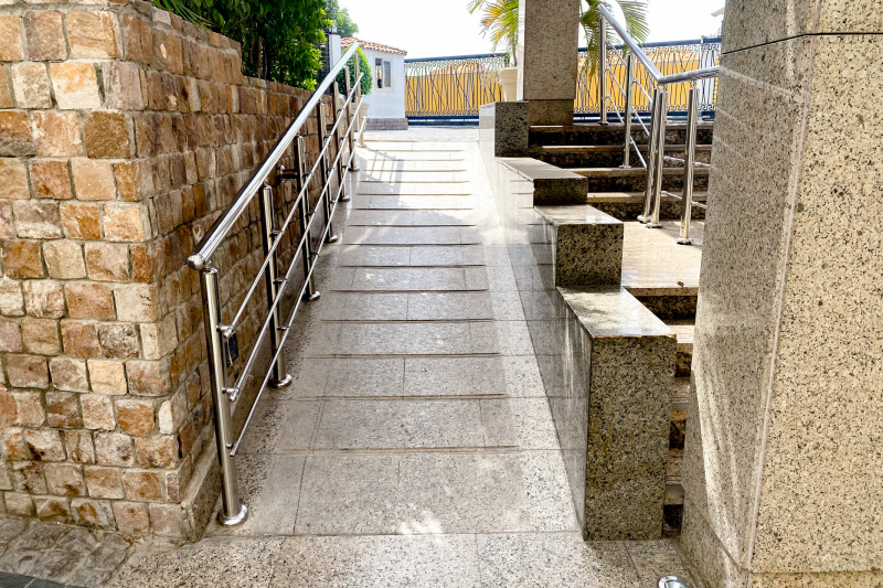 There is a narrow ramp with a handrail leading up to a paved area.