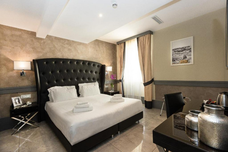 The spacious room has 1 full-sized bed with nightstands on either side. There is a movable chair, a table, a luggage stand and wall-mounted reading lamps.