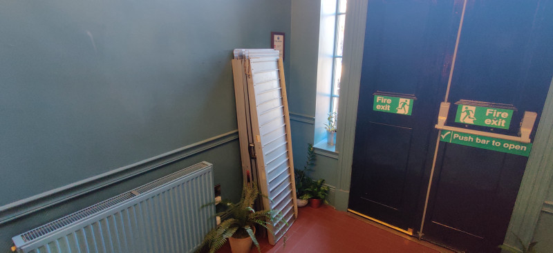 The fire exit has a push-bar to open. The doors are wooden and have windows on either side.