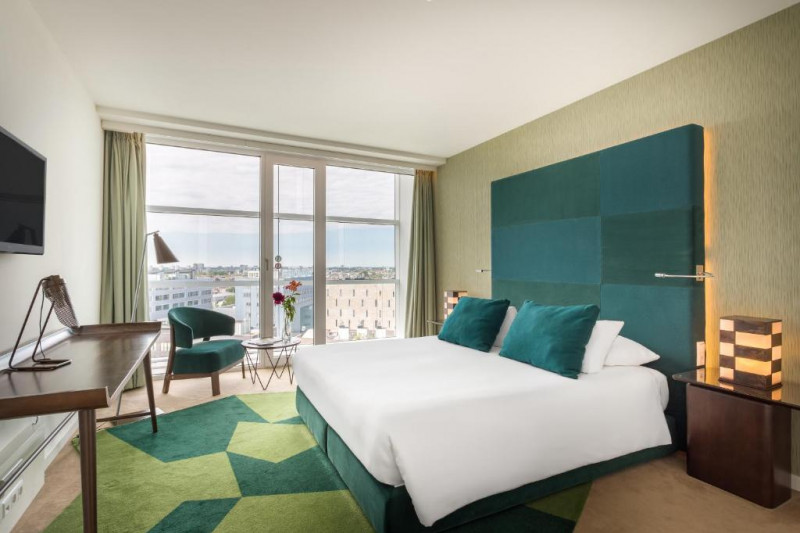 This room has 1 queen-sized bed with nightstands. There is also a small chair, a round coffee table, a wall-mounted TV, and a workstation.