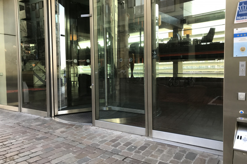 Access to the hotel is through revolving door. To one side, there is an accessible manual glass door.