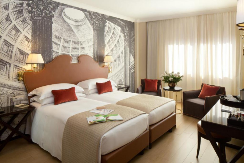 The room has twin beds pushed together with nightstands. There are 2 armchairs with a coffee table, a stool, a and desk.