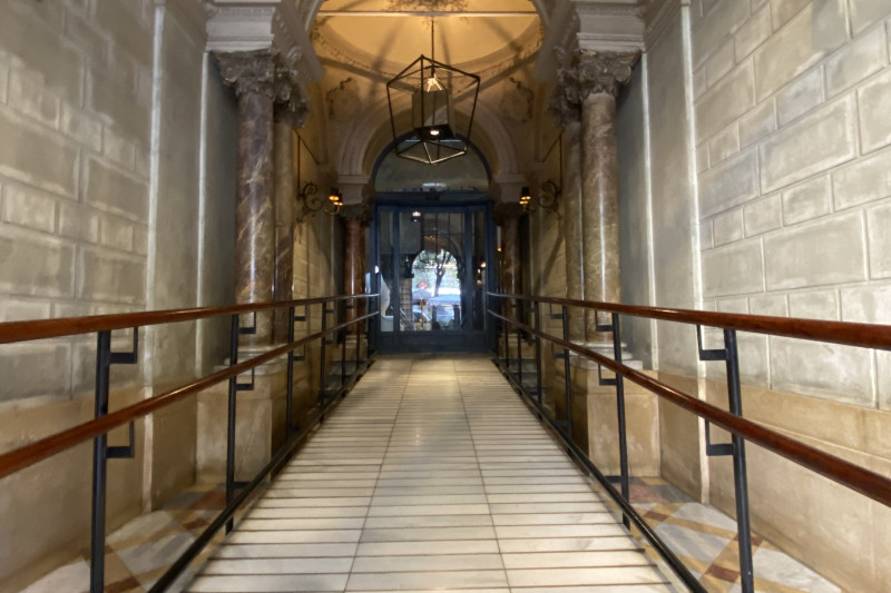 There is a wide ramp with handrails on either side leading from the hotel entrance to a set of big glass doors.