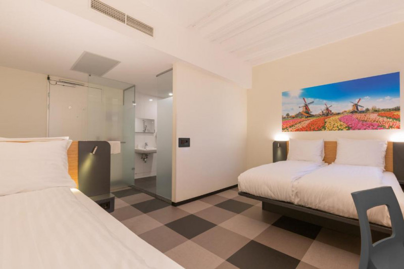 This room has 2 single beds and another bed. There are nightstands on either side of the beds and a movable chair.