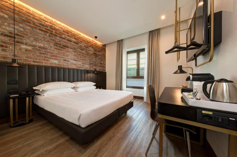 This room has a queen-sized bed with nightstands on either side. There is a workstation, a movable chair and a wall-mounted TV.