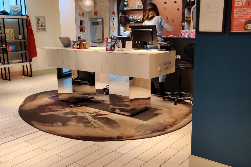 The spacious reception area has an accessible check-in desk. There are shelves against one wall and a drinks fridge on the other side.