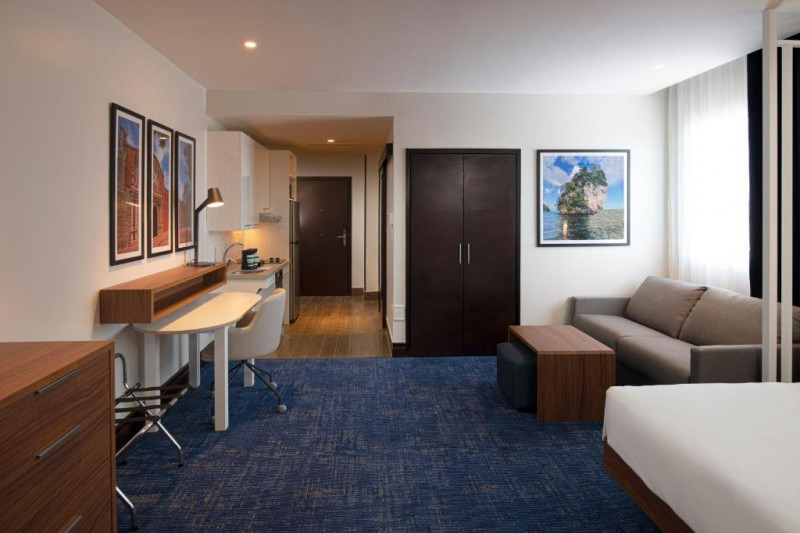 The spacious room has a small kitchen, a workstation with a movable chair, a luggage rack, and a sofa bed. There is also a closet, a coffee table, a chest of drawers, and a bed.