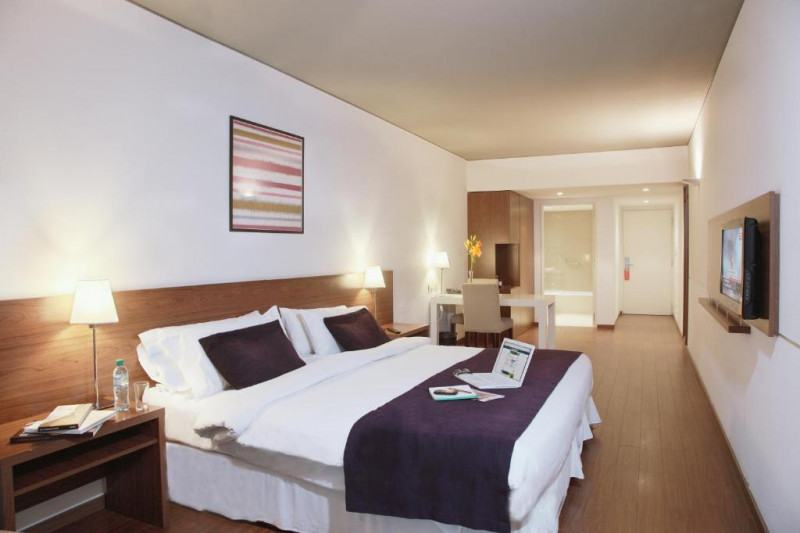 This spacious room has a queen-sized bed with nightstands. There is a wall-mounted TV and a workstation with a movable chair.