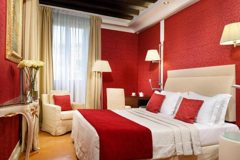 This room has 1 full-sized bed with nightstands. There is a high back chair, an armchair, and a corner table. There is limited floorspace.