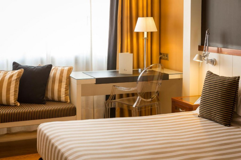 This room has a bed, a workstation, a movable chair and a bench with cushions.