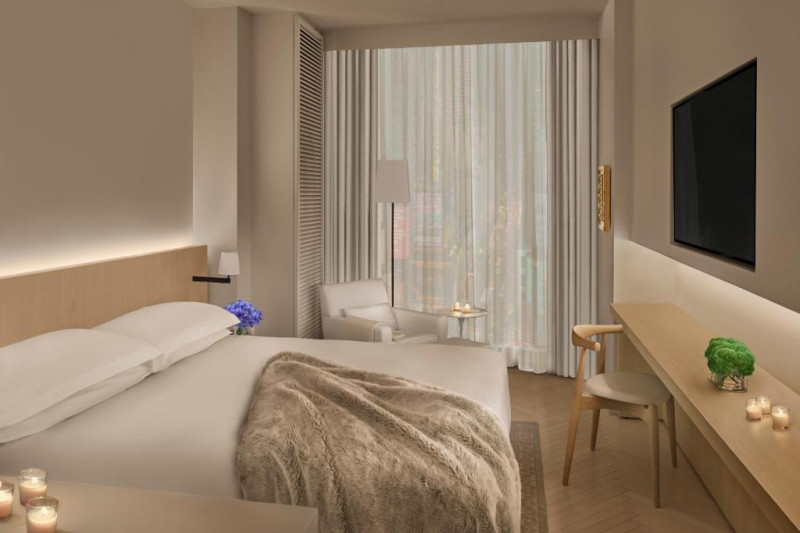 The room has 1 king-sized bed with nightstands, an armchair with a coffee table and a wall-mounted TV. There is a wooden bench with a movable chair.