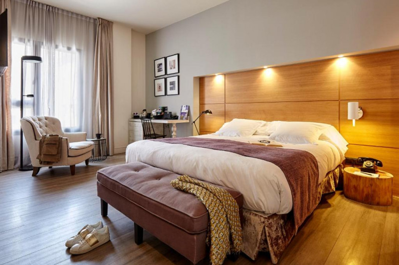 The spacious room has 1 full-sized bed with nightstands. There is a workstation with a movable chair, an armchair, and a plush bed bench.