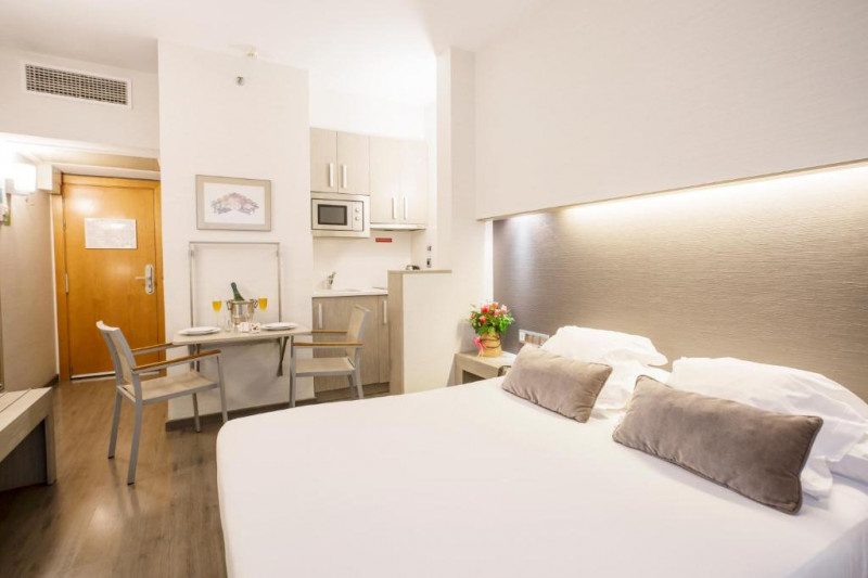 This room has a small kitchen, a table and 2 chairs, and a full-sized bed.