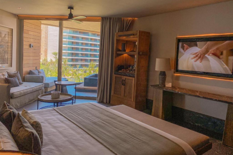 The room has 1 king-sized bed, a sofa and 2 coffee tables. There is a wall-mounted TV and a long marble table with a lamp.