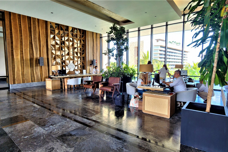 The spacious reception area has check-in desks with chairs in front of them. There are assorted tables and movable chairs around the room.