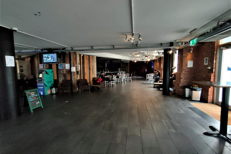 The spacious lobby has assorted tables and chairs. There is a wall-mounted screen and an ATM cash machine.