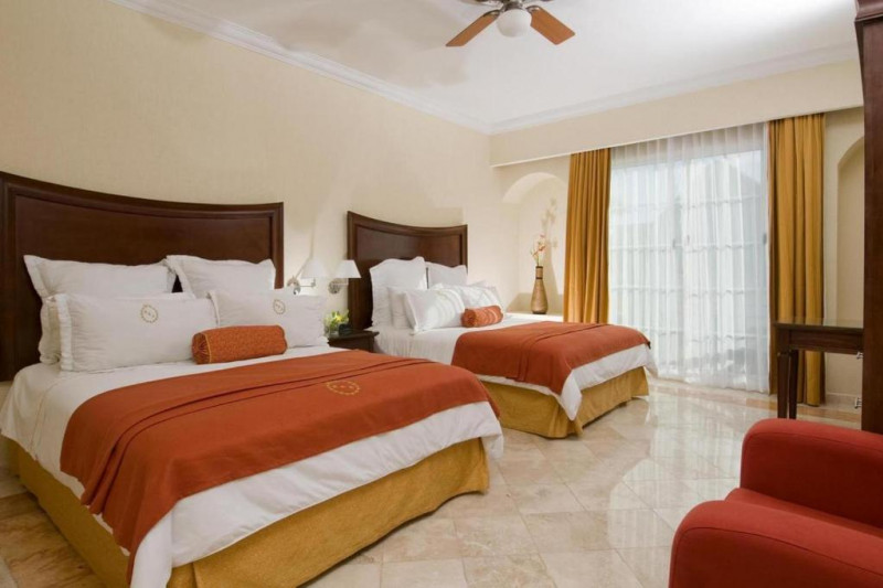 This room has 2 queen-sized beds with a central nightstand. There is an armchair, a workstation, and a electric ceiling fan.