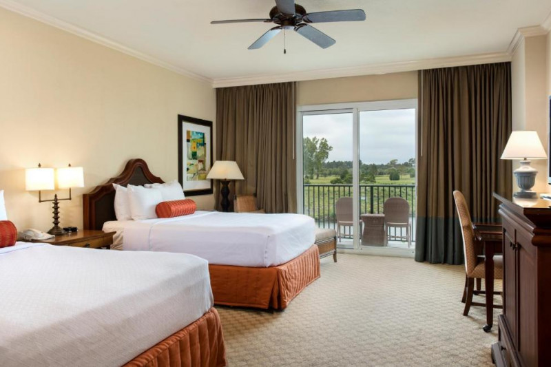 The room has 2 queen-sized beds with a nightstand between them. There is also a workstation with a movable chair and a cabinet with a TV on top.