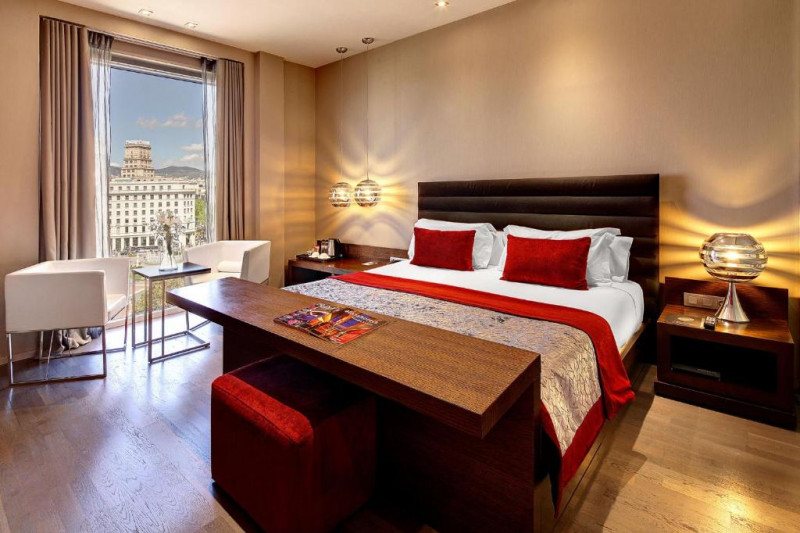 The spacious room has 1 full-sized bed with nightstands. There are 2 armchairs, a coffee table, and a wooden bench with a pouffe at the bottom of the bed.