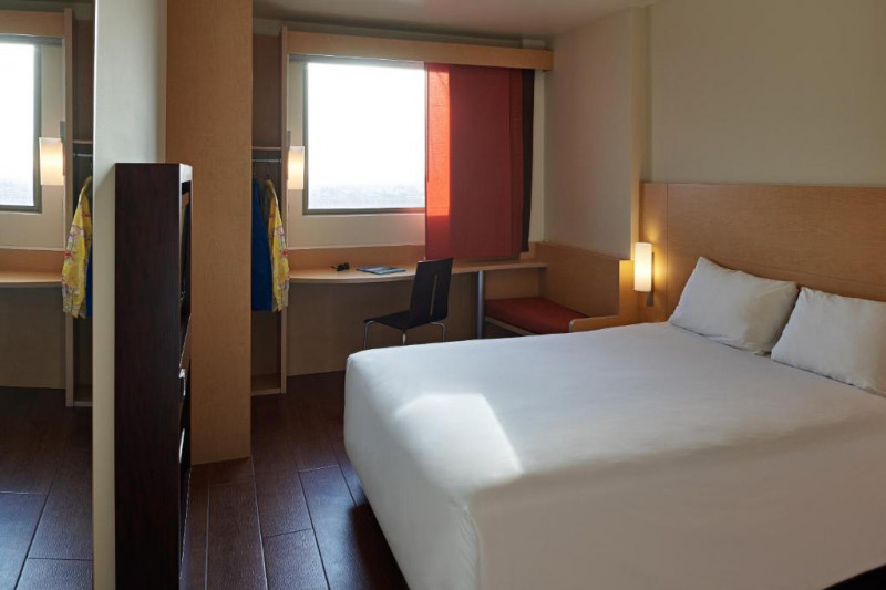 The room has a full-sized bed with nightstands, a closet, a workstation and a movable chair.