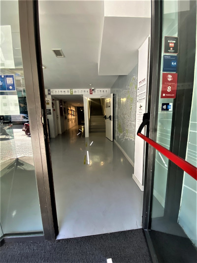 Access to the hotel is through a manual, glass door. There is a spacious lobby and a flight of stairs with a handrail.