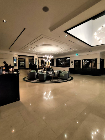 The spacious lobby has armchairs, sofas, and table in the center of the room. There are 5 stairs with handrails leading to another area.
