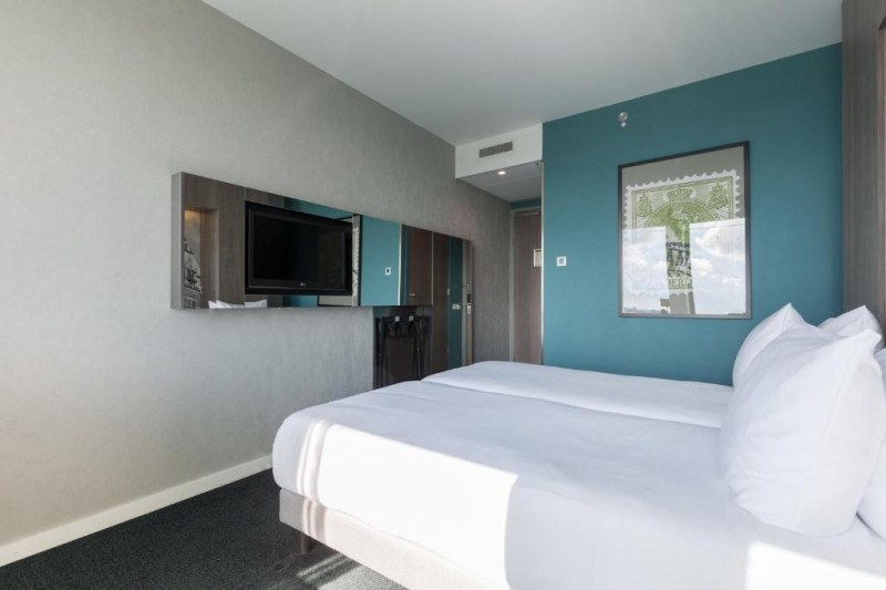 The room has twin beds with nightstands, a wall-mounted TV and a luggage rack.