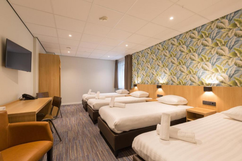 The room has 4 twin beds with nightstands. There is a workstation, 2 chairs, an armchair, a wall-mounted TV, and a closet.