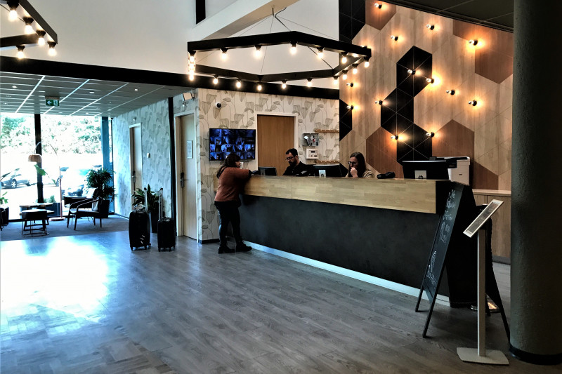 The spacious reception area has a wooden floor and a high check-in desk. There is a carpeted seating area at the far end.