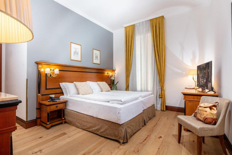The spacious room has twin beds with nightstands. There is a workstation, a TV, and a chair.