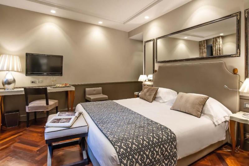 The spacious room has 1 full-size bed with nightstands and a plush bed bench. There is a workstation, a chair, and a wall-mounted TV.
