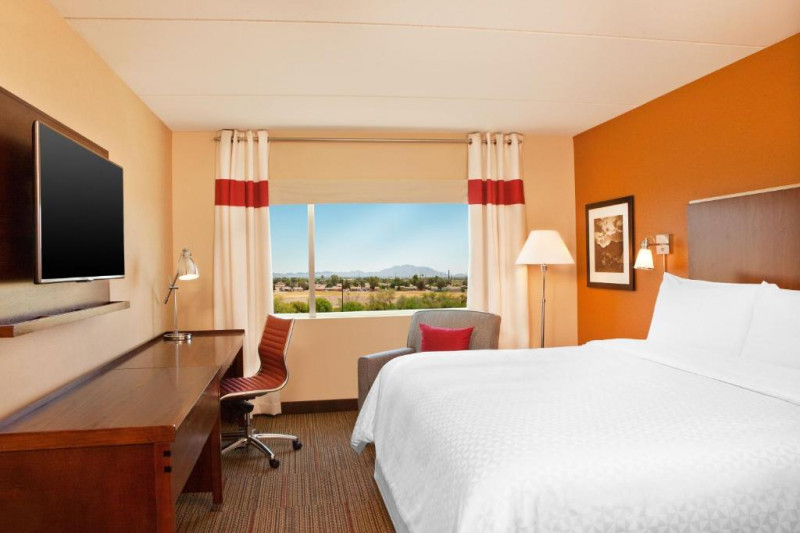 The room has 1 king-size bed. There is a long workstation, a movable chair, an armchair, and a wall-mounted TV.