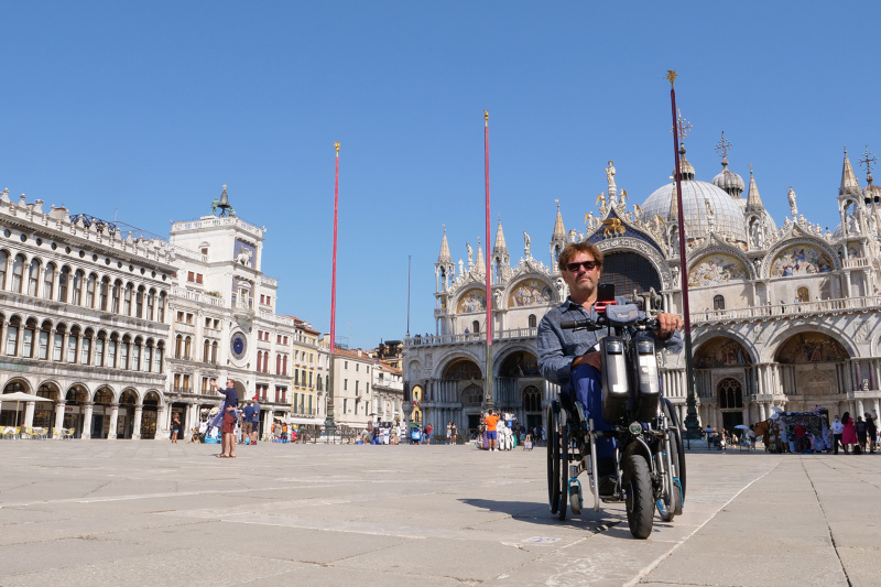 A man in a wheelchair poses in front of the historic St Mark's square