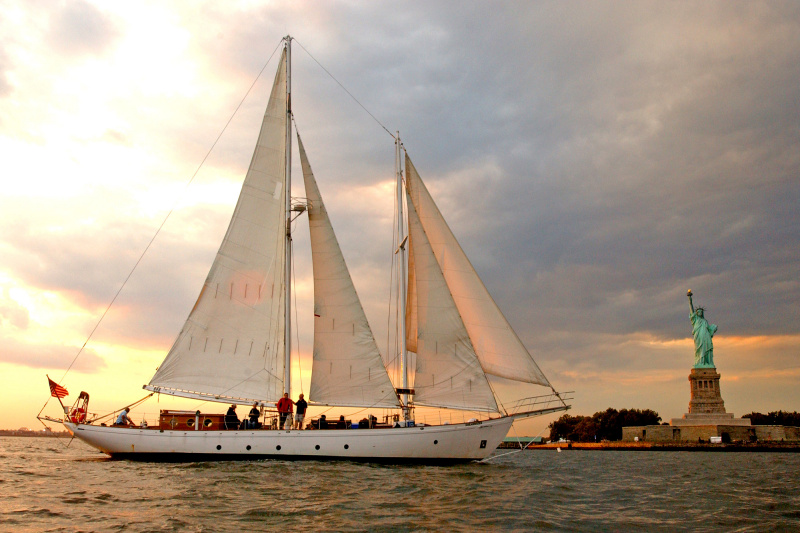 A large white sailing boat in front of the Statue of Liberty