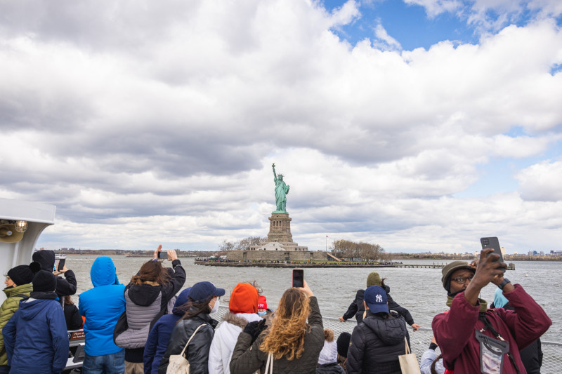 Tourists snap photos of the Statue of Liberty from across the river.